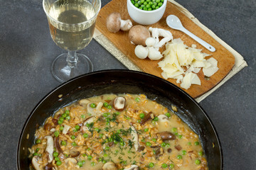 Risotto with mushrooms and green peas. White plate, gray background, glass of wine.