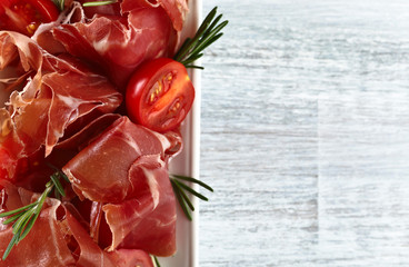  Prosciutto with  rosemary and tomato on a wooden table, free sp
