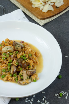 Risotto with mushrooms and green peas. White plate, gray background, glass of wine.