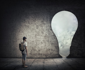 Conceptual image with a person standing in a dark room, in front of a bulb shaped doorway. Escape...