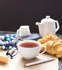 French croissant, glasses, tea and notebook. Workplace concept