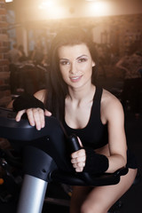 Fototapeta premium Muscular young woman wearing sportswear training on exercise bikes in gym. Intense cardio workout.