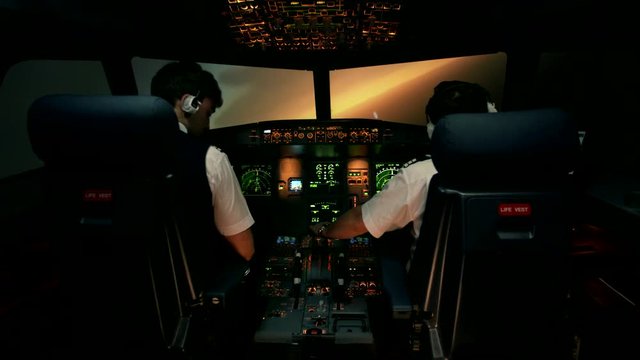 Modern passenger plane change course and start to descent. Sunset view from the cabin of modern plane to the Airport ruway with lighting. Two professional male pilots in the cockpit or flight deck