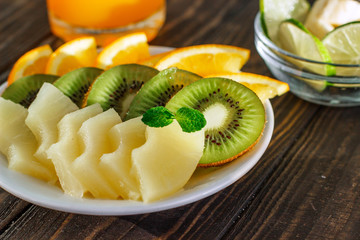 healthy eating plate of fresh fruit orange, kiwi, pineapple in a bowl on a wooden table