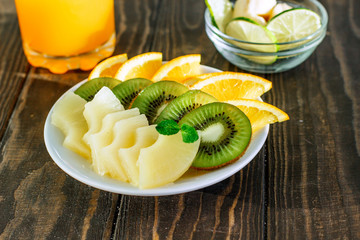 healthy eating plate of fresh fruit orange, kiwi, pineapple in a bowl on a wooden table