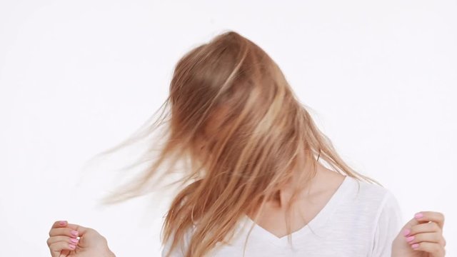 Young beautiful Caucasian blonde girl waving hair and head smiling on white background in slowmotion
