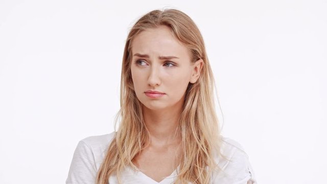 Sad young beautiful Caucasian blonde girl trying not to cry on white background in slowmotion