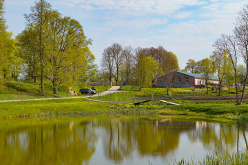 Fototapeta premium View of local farm with pond, green trees, house and hills