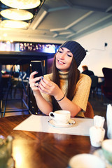 Portrait of beautiful girl in hat using her mobile phone in cafe. Tonned. Selective focus.