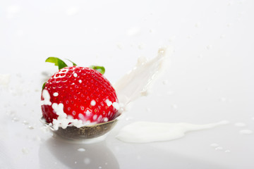 Strawberry falling into spoon full of cream