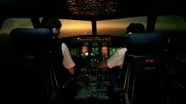Modern passenger aircraft during descent. Sunset view from the cabin of modern plane to the Airport ruway with lighting. Two professional male pilots in the cockpit or flight deck control airplane