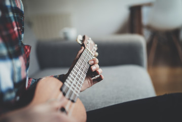Close-up of young girl learning to play ukulele guitar at home, close-up of female hands playing guitar at vintage loft, film effects
