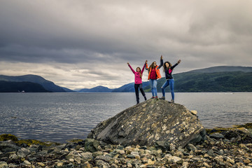 Group of attractive and funny girls on the stone near by fjord,
