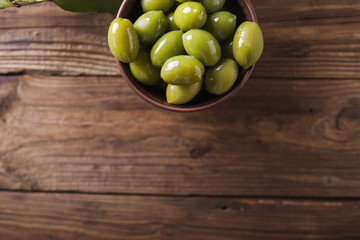 Green olives in a ceramic bowl on a wooden background. Background of olives. Background with green olives. Olives. Copyspace. Green olives and branch of bay leaf. Bay leaf. Copyspace