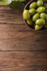 Green olives in a ceramic bowl on a wooden background. Background of olives. Background with green olives. Olives. Copyspace. Green olives and branch of bay leaf. Bay leaf. Copyspace