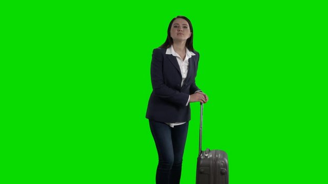 Cheerful woman with luggage waving her hand saying hello against green screen 