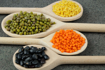Various types of lentils and black beans on wooden spoons.
