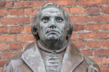 Bronze statue of the reformer Martin Luther in front of a brick wall