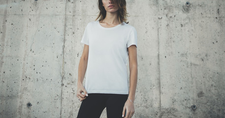 Naklejka premium Pretty young fit girl wearing blank white t-shirt with copy space for your logo or design, mock-up of template t-shirt, concrete grey wall in the background