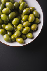 Green olives in a white bowl on a black background. Background of olives. Background with green olives. Olives. Bay leaf. Copyspace