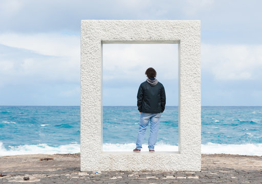 ein junger Mann steht in einem Betonrahmen und schaut auf das Meer