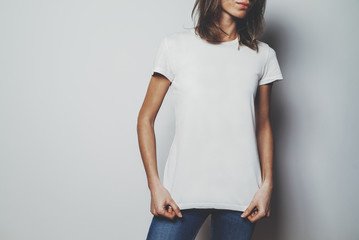 Naklejka premium Young hipster girl wearing blue jeans and blank white t-shirt with area for your logo or design, mock-up of white t-shirt, white wall in the background
