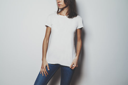 Young hipster girl wearing blue jeans and blank white t-shirt with empty area for your logo or design, mock-up of white cotton t-shirt, white wall in the backround