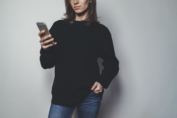 Young pretty girl using modern smartphone device and wearing blank oversize hoodie with space for...