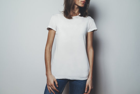 Young pretty girl wearing blank white t-shirt with space for your logo or design, mock-up of white cotton t-shirt, white wall in the background