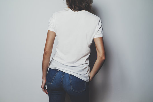 Mock-up of white t-shirt, young hipster girl wearing blue jeans and blank white t-shirt, back view, white wall in the background