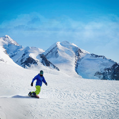 Male snowboarder on the slope with mountain peaks on background