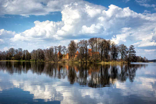 Medieval Trakai castle hidden behind the trees and reflected in water of lake Galve.