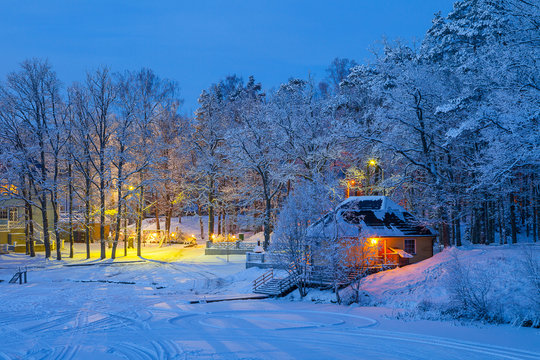 Snowy winter scene of illuminaned cottages in foresr near frozen lake