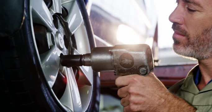 Portrait of mechanic fixing a car wheel with pneumatic wrench in garage 4k