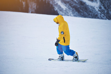 Snowboarder in bright yellow jacket and blue pants rides down on snow slope at sunny winer day in mountain ski resort