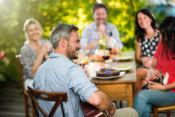 Summertime, man playing guitar for his friends on a terrace