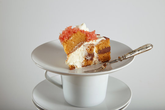 Close shot of piece of cake on small ceramic saucer next to silver dessert fork, isolated on white