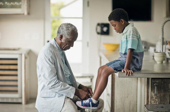 Grandfather tying shoelace of his grandson at kitchen - Powered by Adobe