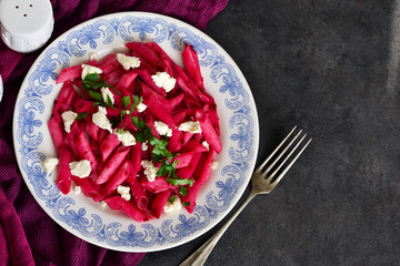 Pasta with beet sauce and feta cheese on a black background