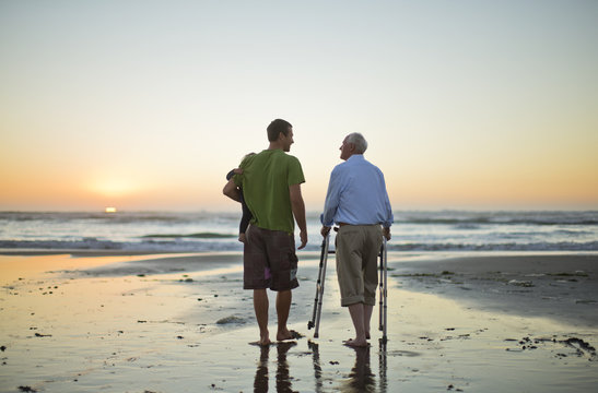 Senior man with a walking aid on the beach with his son and grandchild.