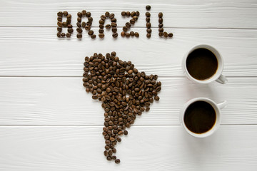 Map of the Brazil made of roasted coffee beans laying on white wooden textured background with  two cups of coffee. Space for text