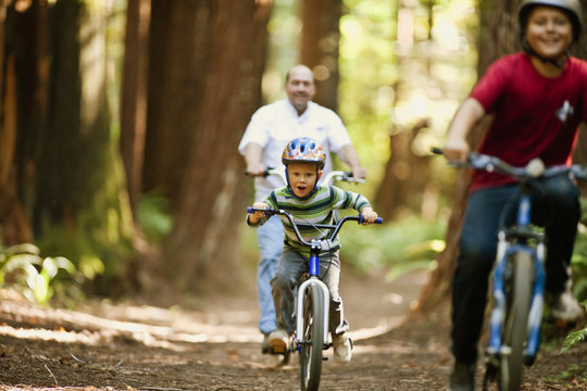 Two boys riding their bicycles with their father through the forest.