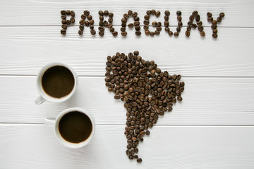Map of the Paraguay made of roasted coffee beans laying on white wooden textured background with two cups of coffee. Space for text