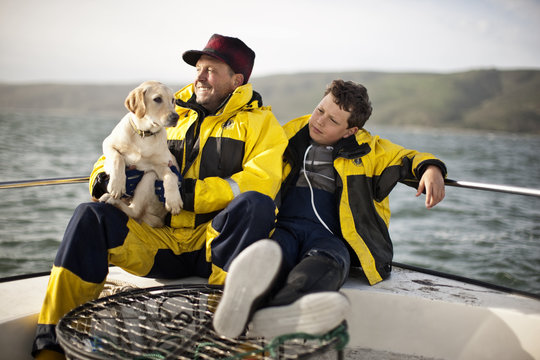 Father sitting with son and holding dog, as they take a break on fishing boat.