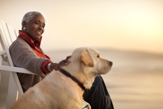 Smiling senior woman petting her dog while sitting on a beach.