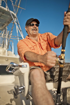 Smiling mature man reeling in a catch on a boat.
