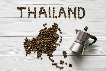 Map of the Thailand made of roasted coffee beans laying on white wooden textured background with two cups of coffee and coffee maker