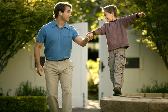 Happy mid adult man helping his son to balance on a stone wall.