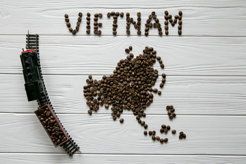 Map of the Vietnam made of roasted coffee beans laying on white wooden textured background with toy train