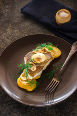 Fried fish with potato and onion on brown plate.